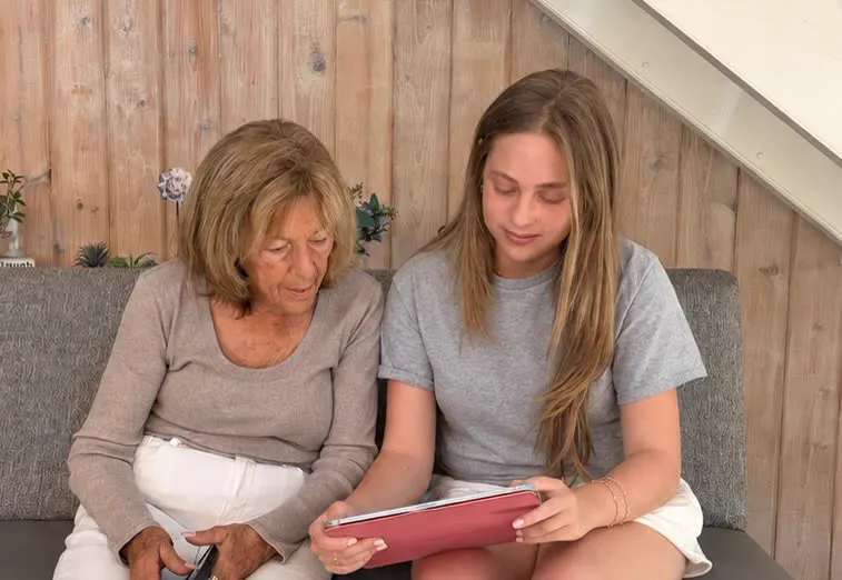A Tech Talk volunteer sitting with a resident, looking at a tablet together